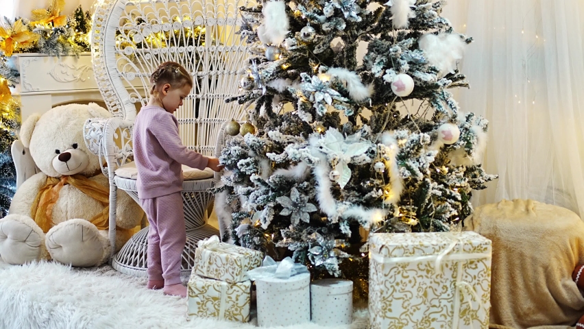 Very nice charming little girl blonde in pajamas near Christmas trees in bright interior of the house. High quality 4k footage | Shutterstock HD Video #1097615727