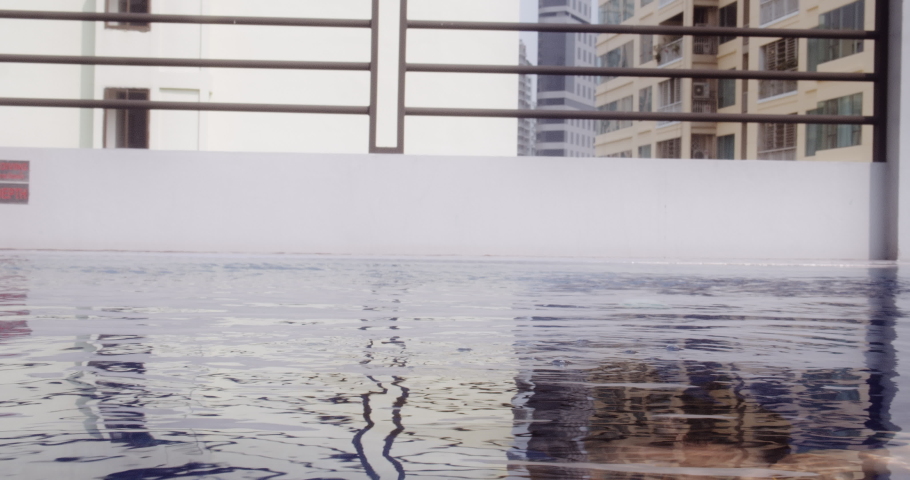 Woman wearing a yellow top smiles and strokes her face and hair after coming out of the pool water.