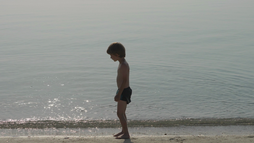Sunset silhouette of happy child going into the sea water