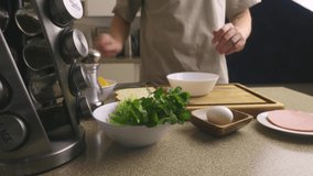 Video. A young man prepares a breakfast of eggs, grated cheese, greens in the home kitchen. On the kitchen table are ingredients, a food processor, dishes. Homemade recipes, family traditions.