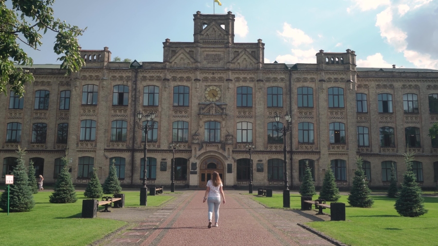 A young, pregnant girl, in sunglasses, walks in a park, lawn area, against the backdrop of the facade of a beautiful, architectural, European building. Jeans, T-shirt. day, sun