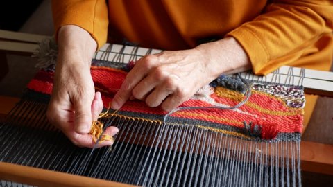 Women's hands using a loom to create a bright tapestry, selective focus. Artisan weaves yellow wool thread. Weaving production Stockvideó