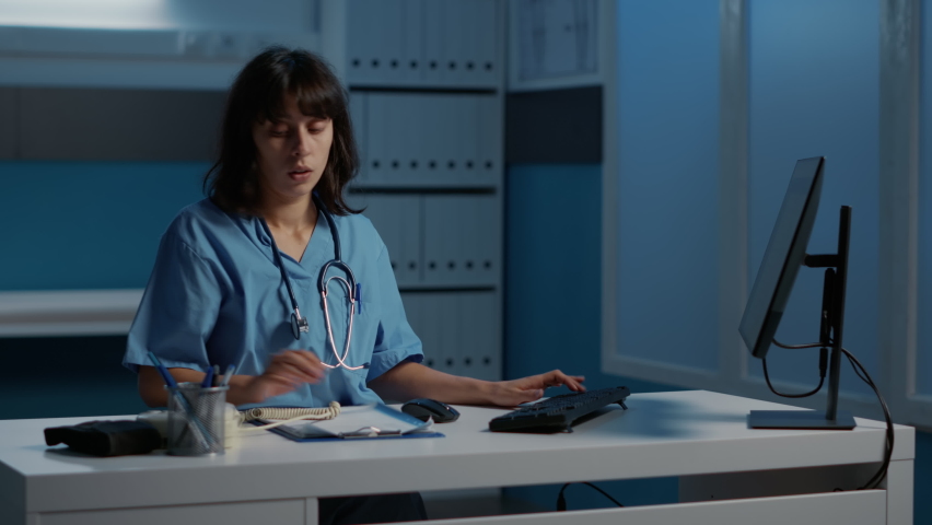 Physician nurse answering landline phone discussing patient report with remote doctor planning medication treatment to cure disease. Medical assistant working over hours in hospital office Royalty-Free Stock Footage #1097625913