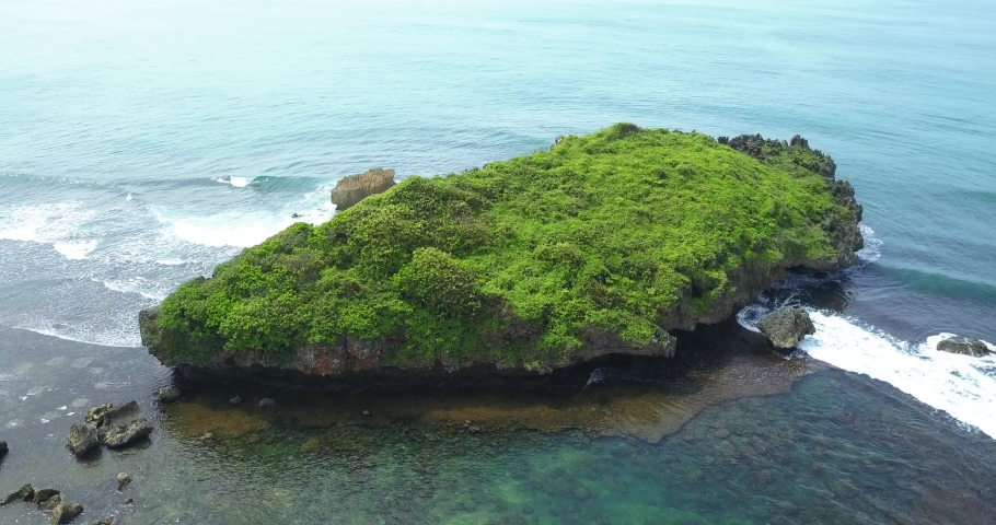 Drone view of huge coral rock with clusters of small rocks that surround it and crushing by the wave