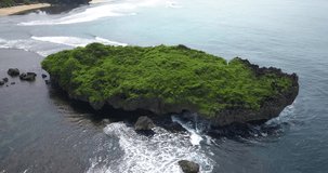 Aerial view of huge coral rock overgrown with grass vegetation on the beach that crushing by the wave