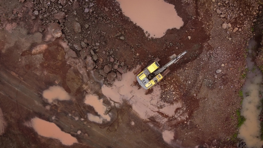 A dynamic top-down aerial footage of an active excavator while working on a quarry site to move dirt and rocks away.