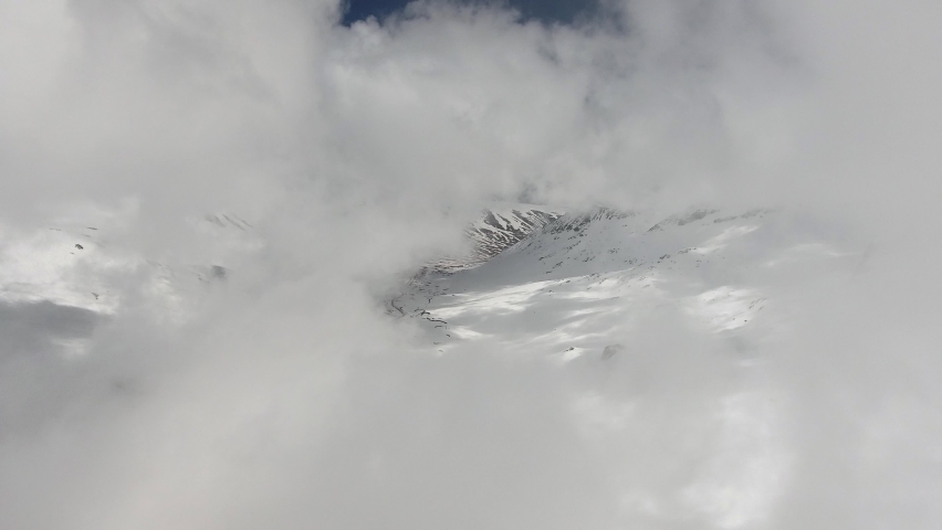 Flying through high-altitude snowy mountain clouds landscape.