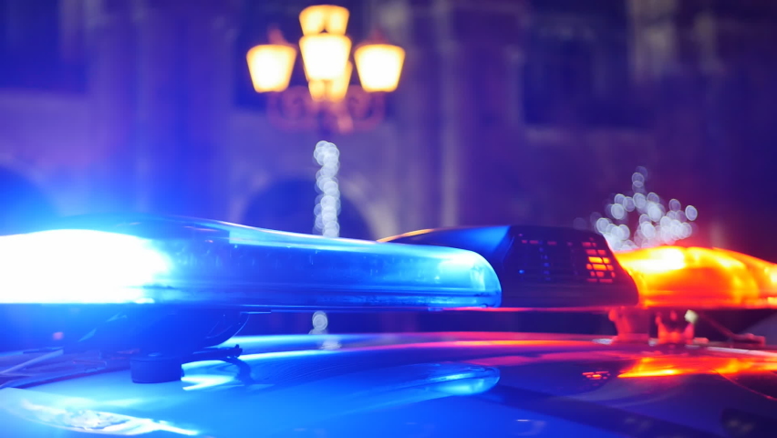 Turned on flasher of a patrol police car at night against the backdrop of city buildings and street lighting lanterns. Red-blue lights blink on the roof of the police car on duty of the police crew | Shutterstock HD Video #1097628993