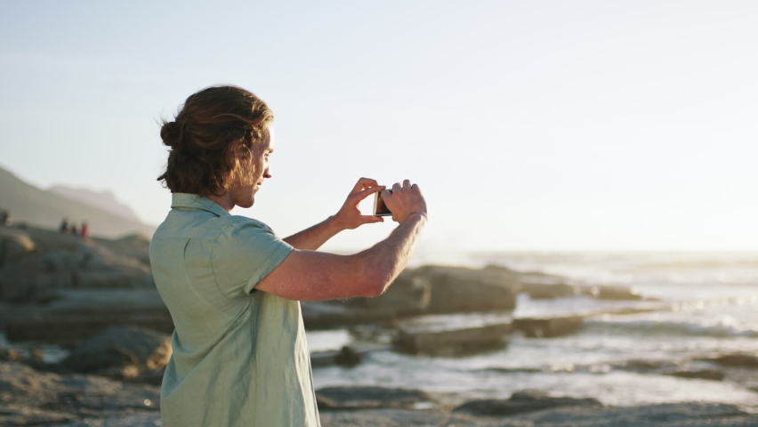 Mobile photography, sea and beach travel of man with a phone looking at nature view with technology. Panorama picture, person and holiday memory of a male on summer vacation at ocean waves at sunrise | Shutterstock HD Video #1097632217