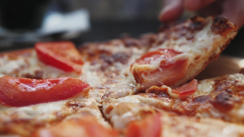 Hand taking salami pizza slice via spatula. Hot melted cheese is stretching, close-up. Fast-food concept.