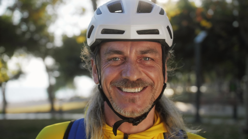 Smiling mature man wearing helmet and sportswear. Bike commuting. Closeup portrait of a happy male cyclist with a helmet in the park. Royalty-Free Stock Footage #1097635327
