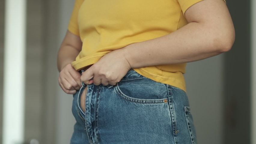 Woman body fat belly. Cropped mid section of an obese woman trying to close the buttons of her jeans against a white background