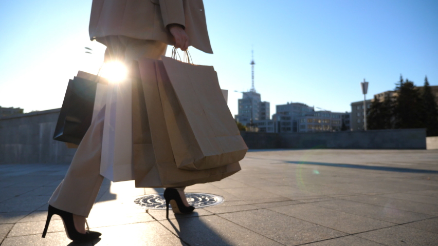 Young woman holds shopping bags walking at sidewalk after purchases. Elegant girl in suit carries paper packets going along sunny urban street. Concept of sales and discounts. Close up Slow motion | Shutterstock HD Video #1097636309