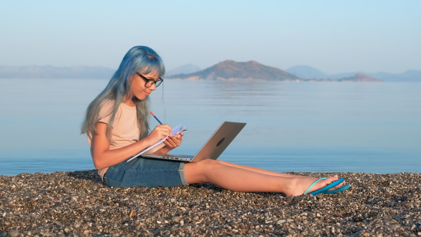 Teen school study by sea. A view of studing teen girl with notebook and laptop against sea scape in the morning.