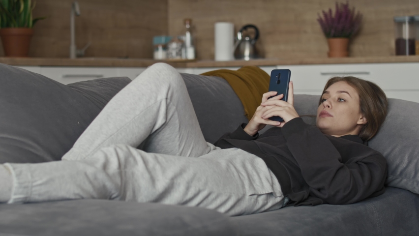 Caucasian woman relaxing on the couch and using mobile phone. Shot with RED helium camera in 8K.    | Shutterstock HD Video #1097638355