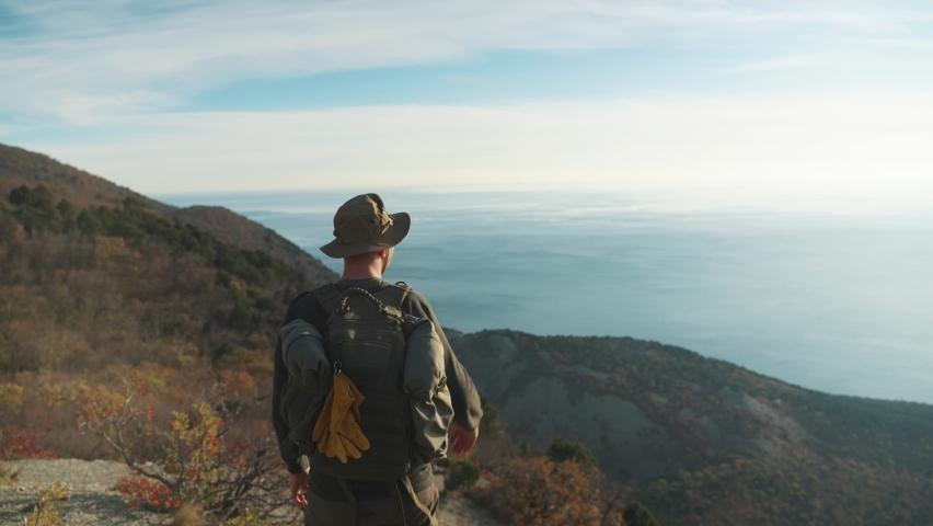 Man traveler in a hat enjoys the view opening from the mountains. Sea, blue sky. Travel concept, hiking, tourism.
