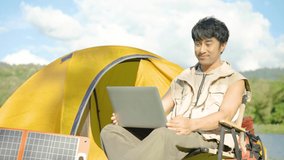 4K, Young travel man relax and enjoy talking calling on video on laptop, using laptop computer work remotely anywhere using internet connected to portable solar panel charging 