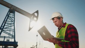 oil business. engineer next to an oil rig. oil industry production finance concept. gas production. a worker with a laptop monitors oil production next to an station. a worker sun in hard hat works - Powered by Shutterstock - Get 15% off with code: PIKWIZARD15
