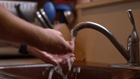 A slow motion video of a man washing his hands with water, in kitchen