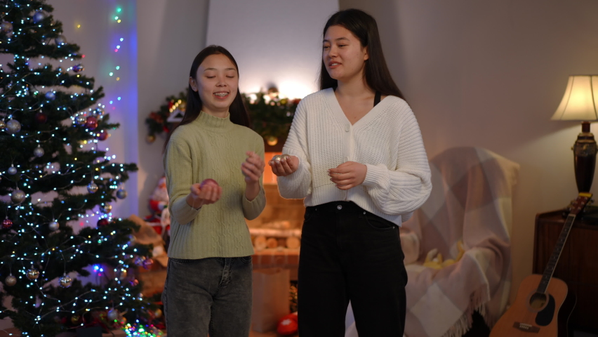 Young slim Asian woman making surprised facial expression listening to rumor as friend whispering on ear sharing gossip. Two young millennial ladies gossiping decorating New Year tree on Christmas eve | Shutterstock HD Video #1097654099
