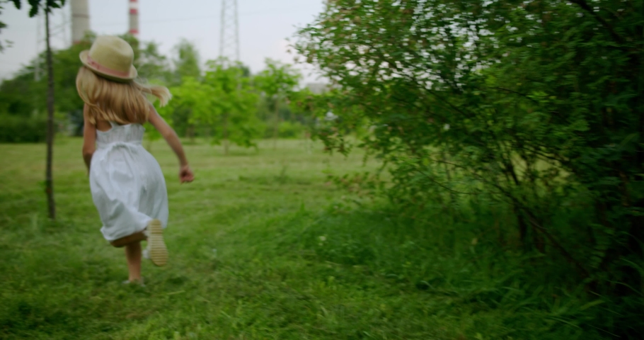 Girls running in green summer park. Tracking shot of little sibling girls in summer dresses and straw hats playing chasing game and running on green meadows with trees in park  Royalty-Free Stock Footage #1097660605