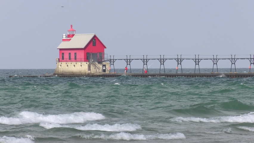 Outer lighthouse on Lake Michigan at Grand Haven. Square red structure with catwalk and breakwater. Static shot with rough waves in foreground. Shot on a partially overcast day.