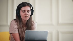portrait of young beautiful woman with headphones chatting by video call at home, looking at tablet, teen girl is calling online, distant communication by social media and mobile application