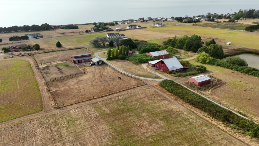 Aerial view of a classic red barn with a horse and harvested fields nearby.
