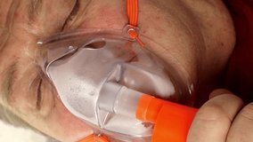 Sick middle-aged man is breathing through oxygen mask while lying in bed. Treatment of asthma, allergies, bronchitis, pneumonia in Covid-19 and respiratory diseases.