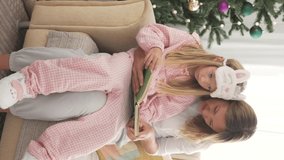 Mother and daughter read a New Year's fairy tale at home by the Christmas tree.