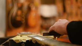 Cropped video of a master guitar luthier hands polishing the frets on the fretboard of the black electric guitar in a repair service shop. Manufacture in a small workshop. Music instrument maker.