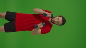 Vertical Video,Vertical View.Portrait of Young Angry Professional Bearded Fighter Making Boxing Exercises iwith Dumbells straight to the Camera on a Green Screen, Chroma Key.Healthy Lifestyle Concept.