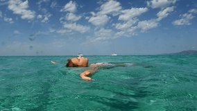 Little red hair girl relaxes by floating with open arms and letting herself be lulled by sea movement. Low angle underwater pov