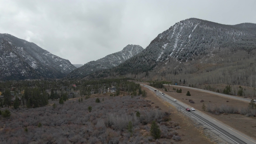 Aerial dolly shot following along Interstate 70 with fresh snow on distant mountains. Filmed with a drone in the Town of Frisco Colorado during the winter.