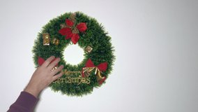 The hand of a man adjusting a Christmas wreath on the wall - Powered by Shutterstock - Get 15% off with code: PIKWIZARD15