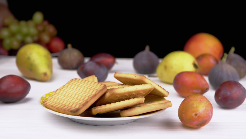 Hands Taking a Plate Cookies and Putting a Dish of Grapes with Plums on Table. Juicy ripe grape of red and green color on blurred fruits background. Pears. Healthy food and junk food concept. Harvest.