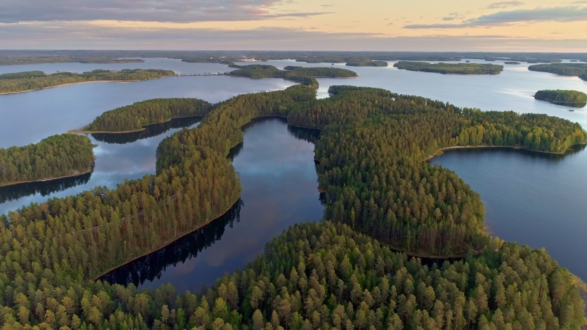 Flying over lakeland in Finland. Aerial shot of many green islands at sunset - classical Finnish landscape. Finnish Lake land in sunset lights. Green islands and lake with clouds reflection. 4K, UHD