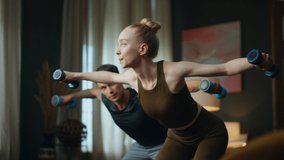 Young family doing gym exercise with dumbbells at home. Sporty attractive couple making hands swing with weight. Slim blond woman training arms strength with athletic man. Partners workout together. - Powered by Shutterstock - Get 15% off with code: PIKWIZARD15