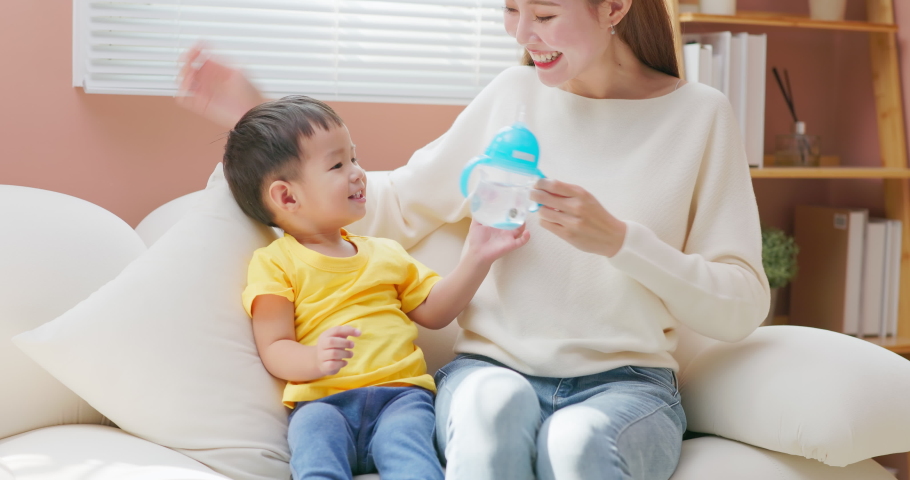 Asian young happy mother is looking to her son while he drinking water from the kettle at home | Shutterstock HD Video #1097711793