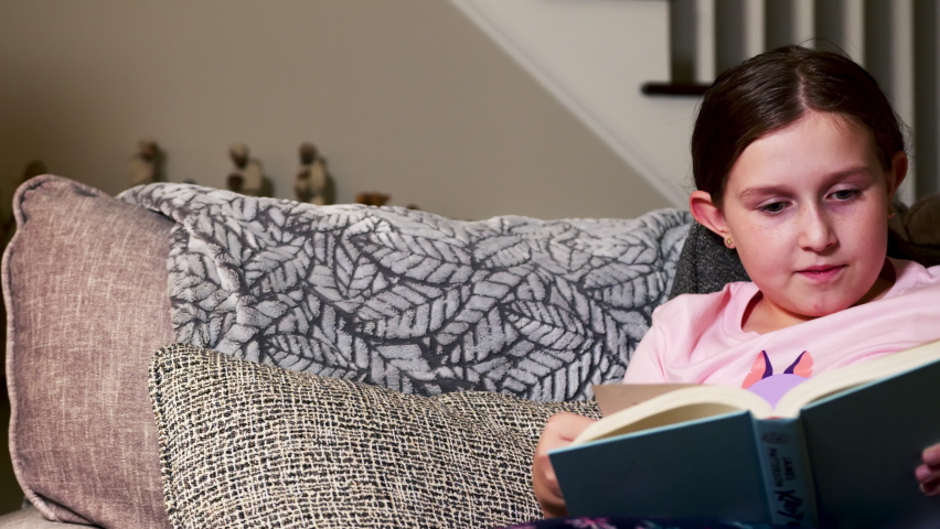 Young girl reading book in living room. Panning left to right. | Shutterstock HD Video #1097715103