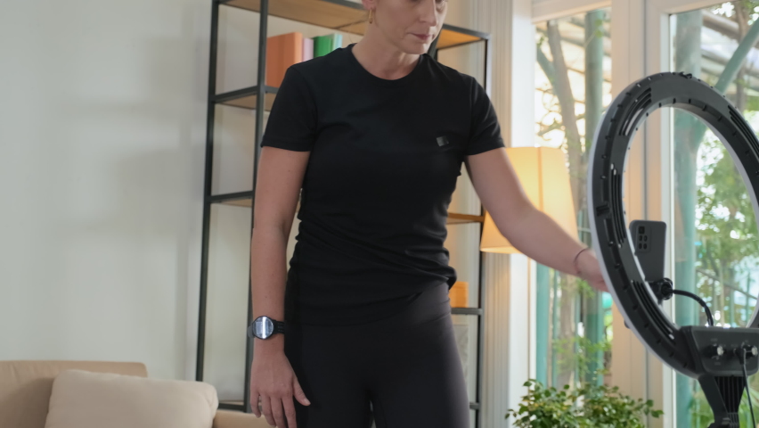 Female fitness influencer turning on ring light and smartphone camera while preparing for filming video workout or online streaming from home | Shutterstock HD Video #1097717413