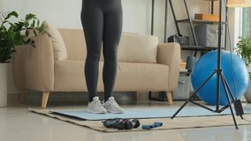 Tilt up shot of female fitness coach with headset explaining exercises in front on smartphone and ring light while filming video class or training online from home
