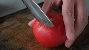 Chef hands cutting a fresh tomato with knife on wooden board. Cooking vegetarian salad in kitchen. 4k video