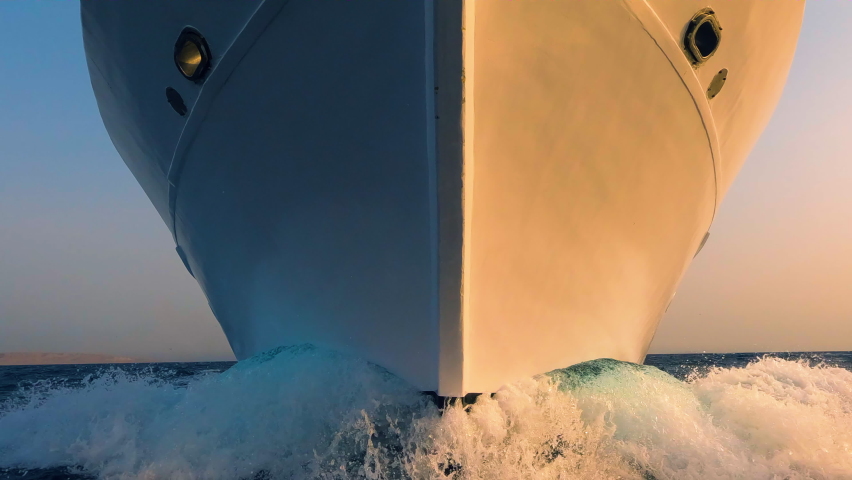 Sailboat prow and white foam water splashes close up front view. Yachting, ocean sailing, sunrise sun light on vessel forepart, boat bow closeup