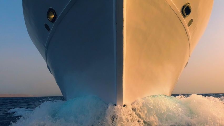 Sailboat prow and white foam water splashes close up front view. Yachting, ocean sailing, sunrise sun light on vessel forepart, boat bow closeup