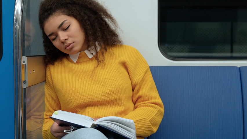 African female sleeping in the subway holding a book in his hands, a young students goes to study at the university, public transport.