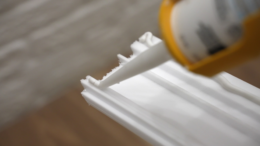 Process of applying white glue on white baseboard surface to fix to the wall, sticky adhesive glue for apartment plinth installation, using glue tube for fixing objects at home. High quality 4k Royalty-Free Stock Footage #1097724743
