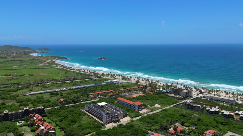 Aerial view of the Hotels on the Playa El Agua tropical beach on the Margarita island. Turquoise water of the Caribbean big waves and clear blue sky. Vacation in beautiful Venezuela Royalty-Free Stock Footage #1097727121