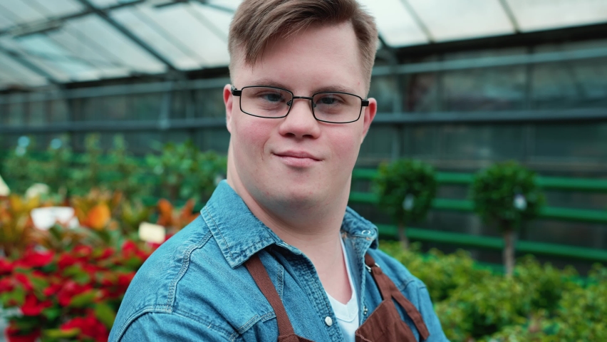 Handsome male florist with down syndrome looking at the camera in the greenhouse Royalty-Free Stock Footage #1097732499