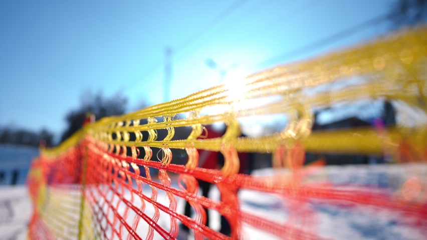 Close-up red and yellow fence on ski resort in sunshine outdoors. Safety border on winter resort in sunlight with people shadows passing in slow motion